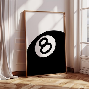 May include: A framed art print featuring a black and white design. The artwork showcases a stylized eight ball from a game of pool, with the number "8" prominently displayed in a white circle against a black background. The frame is gold-colored.