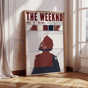 May include: A framed poster featuring the text "THE WEEKND" in burgundy, with "HOUSE OF BALLOONS" below. The artwork includes a stylized portrait and color swatches. The frame is gold, and the poster is leaning against a white wall.
