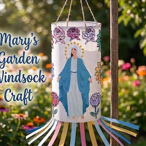 May include: A cylindrical windsock craft featuring a painted religious figure in blue robes, adorned with floral designs. The windsock hangs by twine and has colourful ribbons at the base. Text on the side reads "Mary's Garden Windsock Craft."