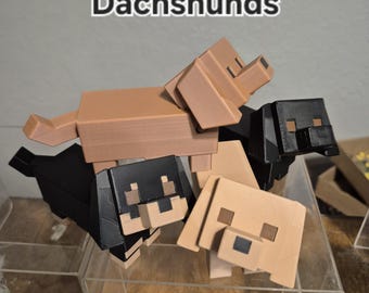 May include: A collection of four blocky, pixelated dachshund figurines in tan and black colours. The figures feature square heads, rectangular bodies, and short legs. The word Dachshunds is printed in white text with a black outline above the dogs.