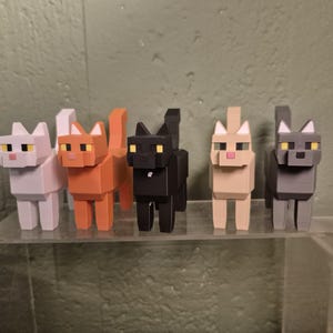 Könnte beinhalten: Fünf blockartige Katzenfiguren im Pixel-Stil, die in einer Reihe stehen. Die Katzen sind weiß, orange, schwarz, beige und grau. Jede Katze hat einen quadratischen Kopf, spitze Ohren, gelbe Augen und eine kleine rosa Nase in geometrischem Design.
