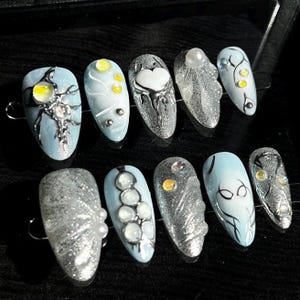 May include: Ten silver and blue nail tips with various designs, including a heart, a spider, and a row of pearls.
