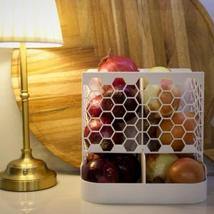 May include: White onion and red onion storage container with a honeycomb design. The container has two compartments and is filled with onions.