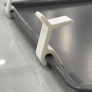 May include: Two white plastic baking sheet clips. The clips are designed to hold baking sheets together.