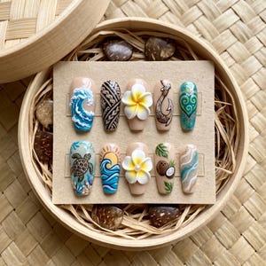 May include: A collection of ten artificial nails featuring diverse designs such as ocean waves, tribal patterns, flowers, and a turtle. The nails are displayed on a beige card within a round wooden container with a woven base.