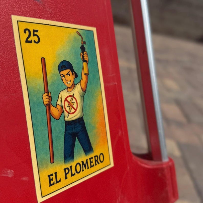 May include: A yellow and blue card with a cartoon illustration of a person holding a wrench and a pipe. The card has the number 25 and the text "El Plomero" on it.