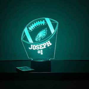 May include: A teal blue 3D printed night light shaped like a football with a Philadelphia Eagles logo and the name "JOSEPH #1" on it.