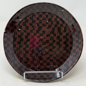 May include: A brown ceramic plate with a black and white checkered pattern. The plate has a glossy finish and is decorated with small white flecks.