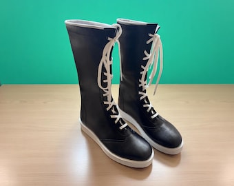 Puede incluir: Un par de botas negras hasta la rodilla con cordones y suelas blancas. Las botas tienen un acabado liso y mate y un diseño sencillo y moderno. Los cordones son blancos y se cruzan en la parte delantera de las botas.