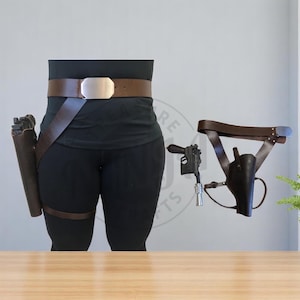 May include: A brown leather belt with a silver buckle, a brown leather holster with a black gun, and a brown leather thigh holster with a black gun.