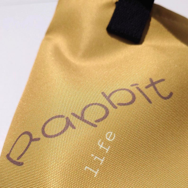 May include: Close-up of a golden-yellow tote bag with the word "Rabbit" in a dark purple font and the word "life" in a white font. The bag has a black handle.