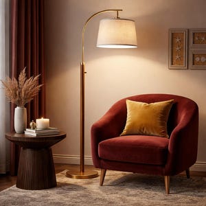 May include: A modern living room scene featuring a burgundy armchair with a gold pillow, a wooden side table, and a brass floor lamp with a beige lampshade. The room has a warm, inviting atmosphere.