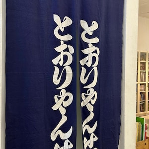 May include: Two navy blue fabric door curtains with white Japanese characters. The curtains are hanging in a doorway. The bottom left corner of the left curtain has the word "madras" in white.