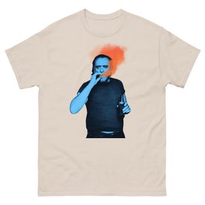 Puede incluir: Una camiseta gráfica azul y naranja con un hombre fumando un cigarro y sosteniendo una botella. El hombre lleva una camiseta azul y pantalones vaqueros.