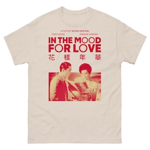 Op de afbeelding: Een beige t-shirt met een rode afbeelding van een filmposter voor "In the Mood for Love." De poster toont een foto van Tony Leung en Maggie Cheung, de sterren van de film, en de titel in Chinese karakters.