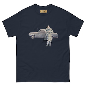 May include: A navy blue t-shirt with a vintage illustration of a man in a trench coat standing next to a car. The text "Old Memories Shirt" is printed in yellow on the shirt.