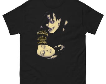 May include: Black t-shirt featuring a vintage movie poster design. The design includes a black and white image of a man with a sinister expression and a woman. The text "Cabinet of Dr. Caligari" is also visible.
