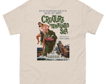 May include: A beige t-shirt with a vintage movie poster design featuring a creature from the haunted sea. The poster has the text "Creature from the Haunted Sea" and "Roger Corman".