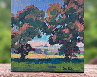 May include: Square canvas painting depicting two large trees with green and orange foliage against a blue sky. The foreground shows a green field, and the background features a colorful landscape. The artist's signature, "Sri Rao," is visible.
