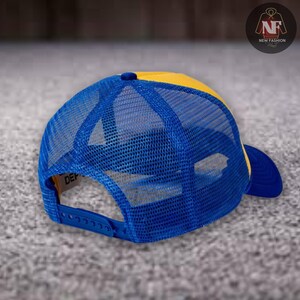 May include: A blue and yellow trucker hat with a mesh back. The hat has a curved brim and an adjustable snap closure. The tag on the side of the hat reads "DEP". The hat is a fashion accessory.