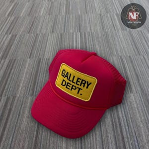 May include: A red and black mesh trucker hat with a yellow patch that says "GALLERY DEPT."