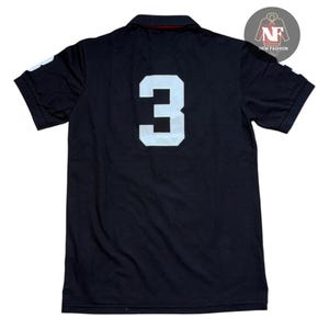 May include: Black polo shirt with a white number 3 on the back. The shirt has short sleeves and a collared neckline. The number 3 is large and centered on the back of the shirt.