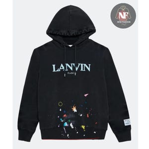 Può includere: Felpa con cappuccio nera con la scritta "LANVIN PARIS" in azzurro sul petto. La felpa con cappuccio ha un cappuccio con coulisse e un design a spruzzi di vernice colorata. Una piccola etichetta sulla manica recita "ART ON A TEE JOSUE THOMAS".