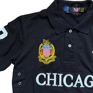 May include: Black polo shirt with white embroidered "CHICAGO" lettering. Features a gold and red embroidered crest with "CHICAGO" text and "RALPH LAUREN" branding. Includes a white number "3" on the sleeve.