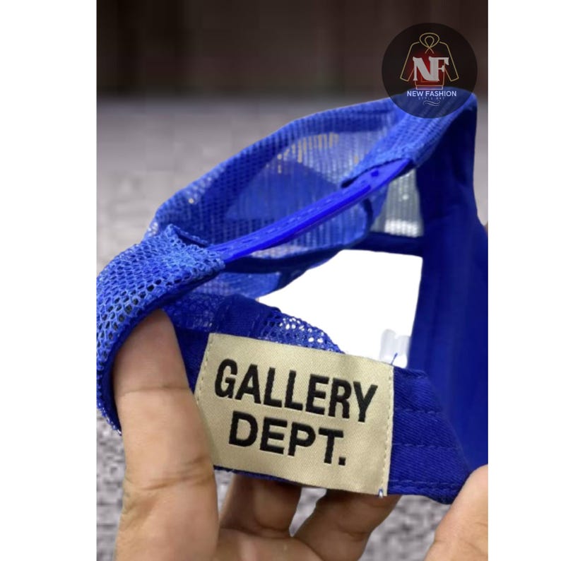 May include: A blue trucker hat with a mesh back and a curved brim. The hat features the text "GALLERY DEPT." on a rectangular patch. The hat has a snap closure for adjustable sizing.