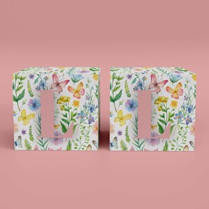 May include: Two white boxes with a floral pattern and butterflies. The boxes have a letter "L" cut out of the front.