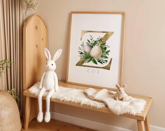 May include: A gold letter Z with green leaves and white eggs, surrounded by a white frame. The name "ZOE" is written below the letter. The image is displayed on a wooden wall.