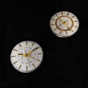 May include: Two vintage watch faces with white dials, gold hands, and gold hour markers. The watch faces have the word "POLJOT" printed on them. The background is black.