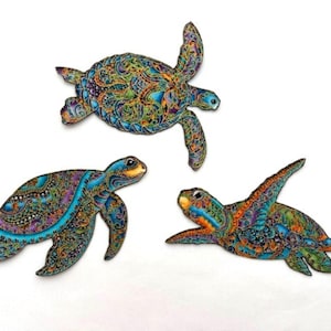 May include: Three intricately designed wooden sea turtles with colorful patterns and blue, green, orange, and purple accents. The turtles are in various poses, with one swimming, one walking, and one with its head up.