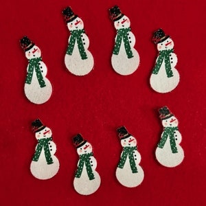 May include: Eight felt snowman ornaments with black top hats, green scarves, and red noses on a red background.