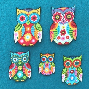 May include: Five colourful owl-shaped fabric patches with intricate floral and geometric designs. The owls feature a variety of bright colours, including red, blue, green, and yellow, with black outlines. The patches are arranged on a teal background.