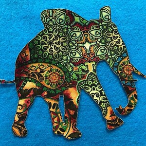 May include: A colorful elephant-shaped cutout with a detailed paisley pattern in shades of green, orange, red, and yellow. The cutout is set against a bright blue background, creating a striking contrast. The elephant's design is intricate.