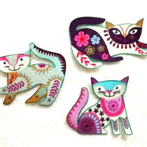May include: Three colorful embroidered felt cat appliques. The cats are in various poses and have different patterns and colors, including teal, pink, purple, and white.