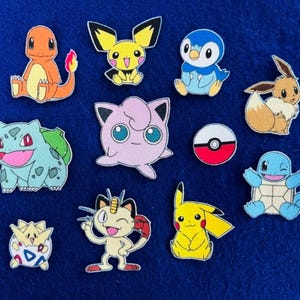 May include: A collection of eleven colorful character patches featuring various creatures including an orange lizard, a yellow mouse, a pink round figure, a blue turtle, and a red and white circular ball, all arranged on a solid blue background.