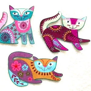 May include: Three colorful wooden cat figurines with intricate patterns and designs. The cats are in various poses, including sitting, lying down, and standing. The colors include pink, purple, blue, green, orange, and yellow.