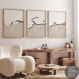 May include: Three framed wall art prints with Arabic calligraphy in black script. Each print has a neutral beige and white color scheme. The frames are a light brown wood. The prints are displayed above a wooden console table.