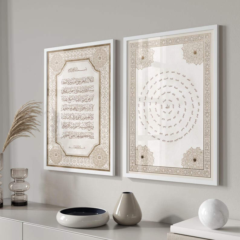 May include: Two framed Islamic art prints with white frames. The prints feature Arabic calligraphy in gold and beige tones. One print displays text, while the other has a circular design. The artwork is displayed on a light gray wall.