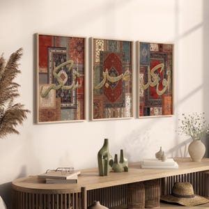 May include: Three framed prints with a collage of colorful patterned rugs and Arabic calligraphy in gold. The prints are hung on a white wall above a wooden table.