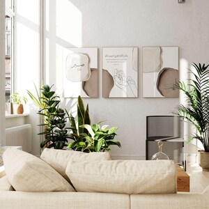 May include: Three minimalist art prints with Arabic calligraphy and abstract shapes in brown and beige tones. The prints are framed in gold and hung on a white wall.