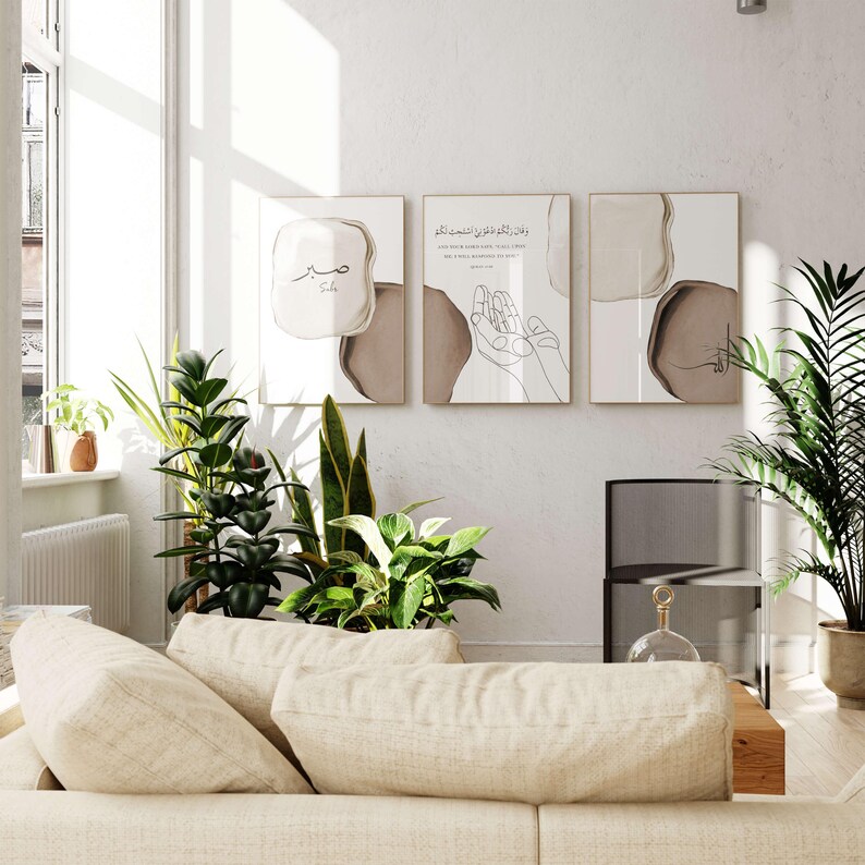 May include: Three minimalist art prints with Arabic calligraphy and abstract shapes in brown and beige tones. The prints are framed in gold and hung on a white wall.