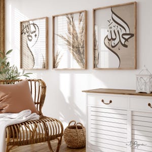 Könnte beinhalten: Drei gerahmte Drucke mit weißem Hintergrund und braunen Akzenten. Der mittlere Druck zeigt ein braunes Kalligrafie-Design mit dem Wort "Allah" in arabischer Schrift. Die Drucke hängen an einer weißen Wand über einer weißen Kommode mit zwei Schubladen.