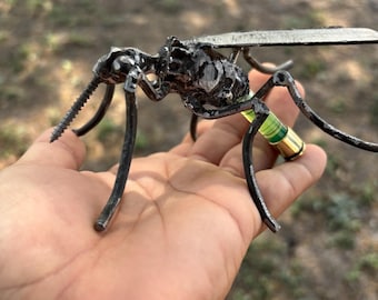 May include: A metal sculpture of a mosquito with a green and gold body. The sculpture is made of recycled metal and is a unique and interesting piece of art.