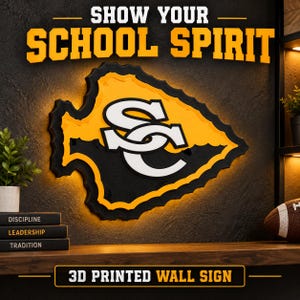 May include: A 3D printed wall sign featuring an arrowhead shape with a black and yellow layered design and a white SC monogram in the center. The sign is illuminated with backlighting and displays the text SHOW YOUR SCHOOL SPIRIT above it.