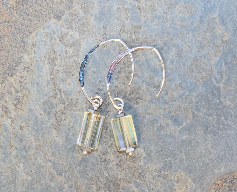 May include: A pair of silver-toned hoop earrings with rectangular, light yellow-green glass beads. The earrings have a curved design with a textured, dark blue accent near the top.