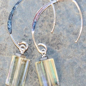 May include: A pair of silver-tone earrings with a curved design. Each earring features a rectangular, iridescent, yellow-green glass bead suspended from a silver wire. The top of the earring has a textured, dark blue and silver accent.