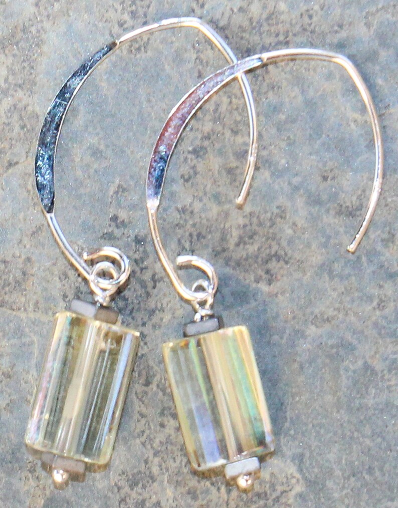 May include: A pair of silver-tone earrings with a curved design. Each earring features a rectangular, iridescent, yellow-green glass bead suspended from a silver wire. The top of the earring has a textured, dark blue and silver accent.